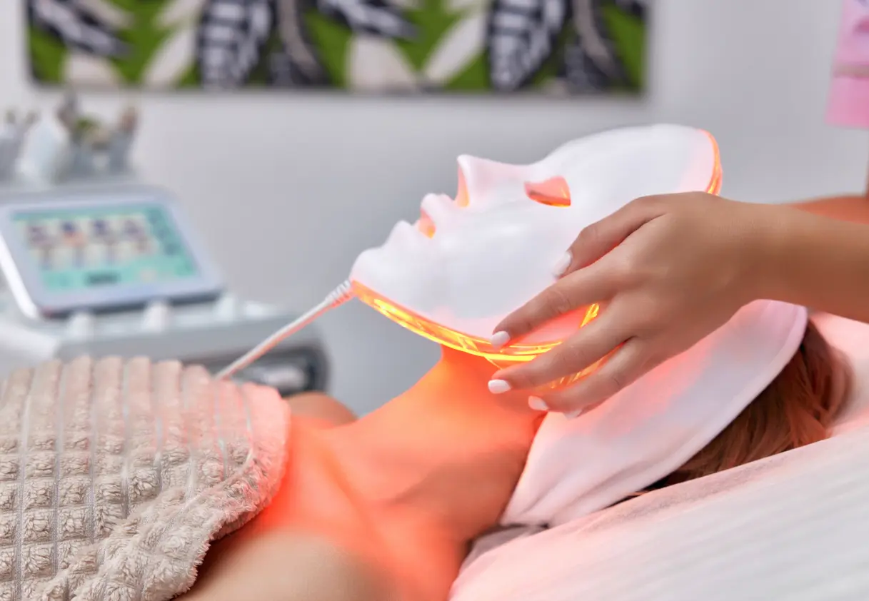 A woman getting facial treatment using red light face mask